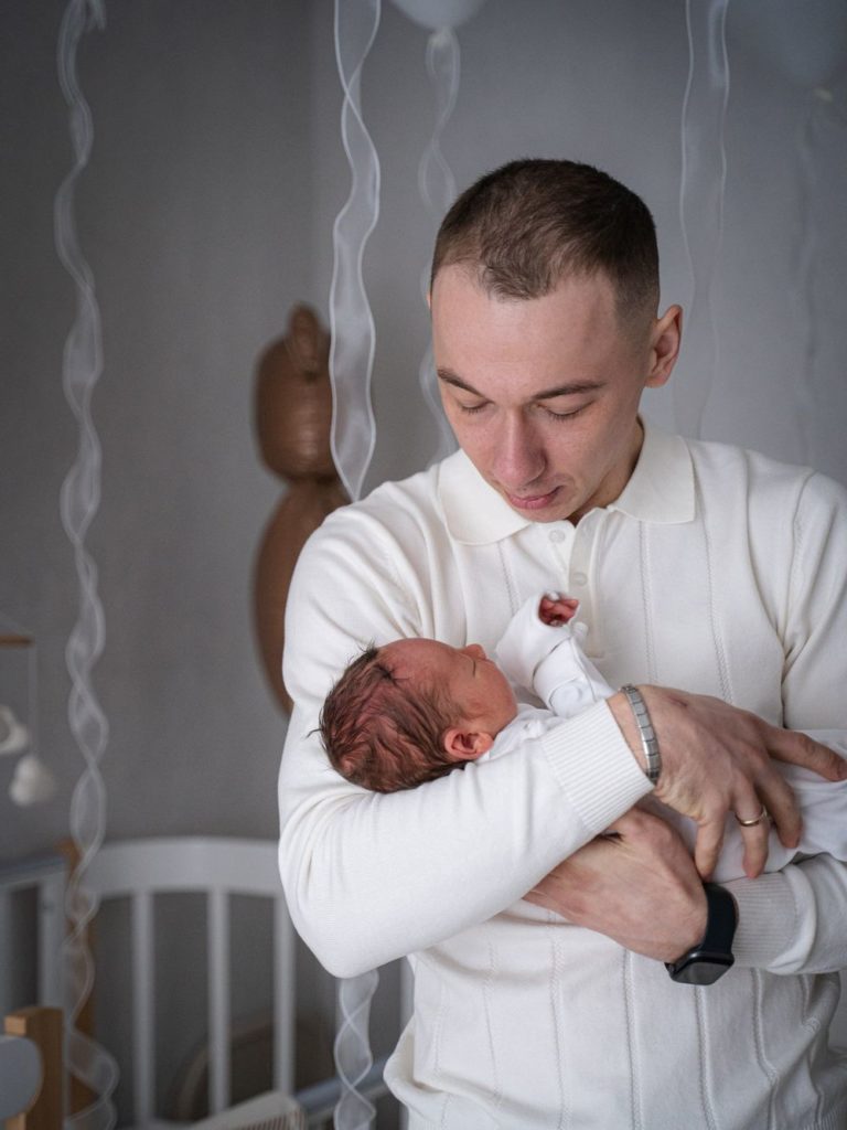 Мужчина в белой рубашке держит новорождённого на руках